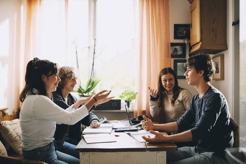 Fröhliche Freunde diskutieren beim gemeinsamen Lernen am Tisch, lizenzfreies Stockfoto