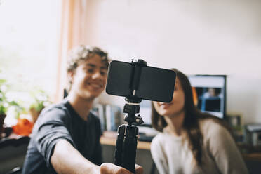 Teenager-Freunde machen ein Selfie mit einem Smartphone auf einem Einbeinstativ, während sie zu Hause sitzen - MASF15491