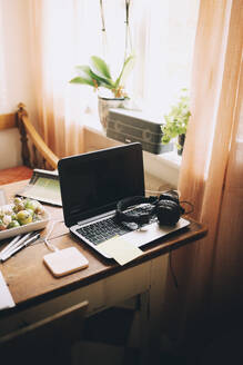 Hohe Winkel Ansicht von Laptop mit Kopfhörern durch Fenster auf Tisch zu Hause - MASF15505