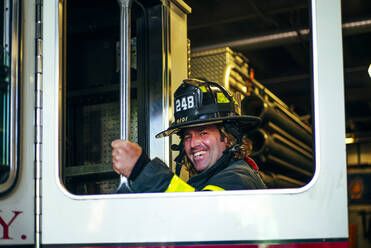 Portrait of happy firefighter getting into fire engine, New York, United States - OCMF00951