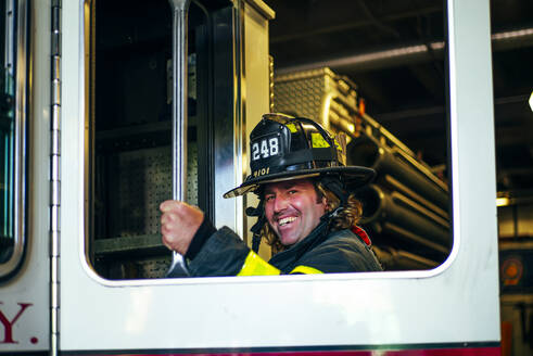 Portrait of happy firefighter getting into fire engine, New York, United States - OCMF00951