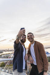 Schwules Paar macht ein Selfie auf einem Aussichtspunkt über der Stadt mit Blick auf den Hafen, Barcelona, Spanien - AFVF04437