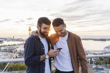 Gay couple using cell phone on lookout above the city with view to the port, Barcelona, Spain - AFVF04438