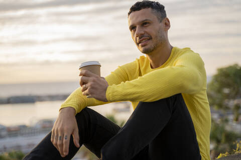 Mann sitzt bei Sonnenuntergang mit Kaffee zum Mitnehmen im Freien, lizenzfreies Stockfoto