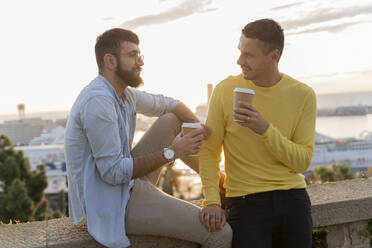 Schwules Paar mit Kaffee zum Mitnehmen auf einem Aussichtspunkt über der Stadt mit Blick auf den Hafen, Barcelona, Spanien - AFVF04451