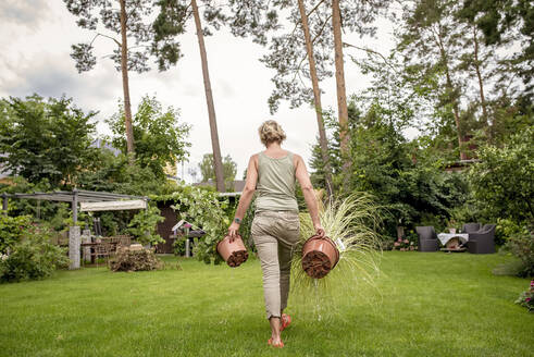 Rückansicht einer Frau, die im Garten mit Pflanzen spazieren geht - BFRF02139