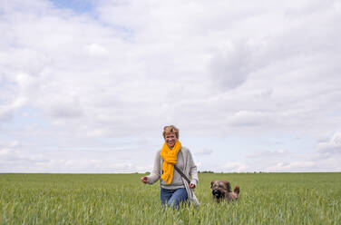 Glückliche Frau geht mit Hund in einem Feld spazieren - BFRF02150