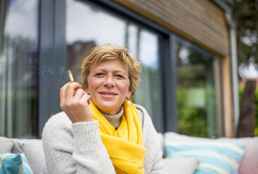 Porträt einer Frau, die auf einer Terrasse zu Hause eine Zigarette raucht - BFRF02152