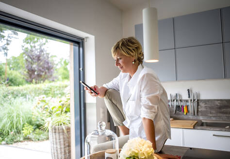 Frau benutzt Smartphone in der Küche zu Hause - BFRF02161