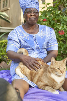 Ältere Frau mit einer Katze auf einer Decke im Garten sitzend - VEGF01075
