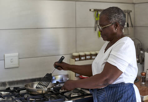 Ältere Frau beim Kochen am Gasherd in der Küche - VEGF01085
