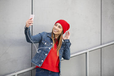 Woman wearing red pullover and wolly hat and taking a selfie - HMEF00694