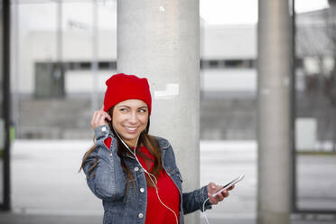 Frau mit rotem Pullover und Schlapphut, die Musik hört - HMEF00696