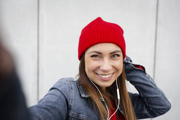 Woman wearing red pullover and wolly hat in front of a wall - HMEF00700