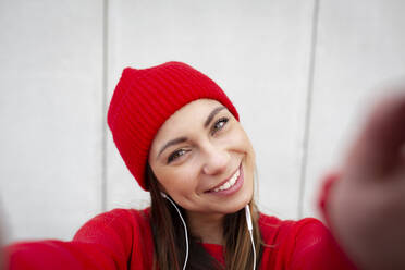 Woman wearing red pullover and wolly hat in front of a wall - HMEF00702