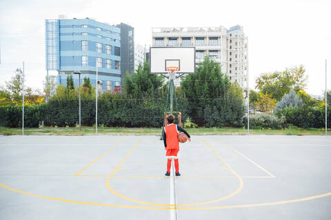 Junge steht mit Basketball auf einem Platz im Freien, lizenzfreies Stockfoto