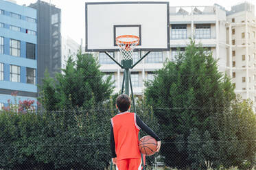 Junge steht mit Basketball auf einem Platz im Freien - JCMF00335