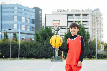 Portrait of smiling boy with basketball on outdoor court - JCMF00337