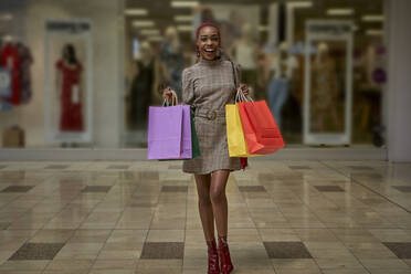 Glückliche junge Frau mit bunten Einkaufstaschen vor einem Geschäft - VEGF01106