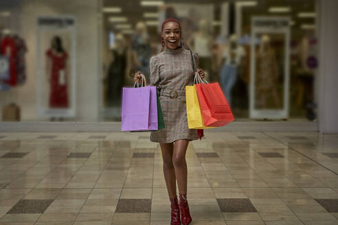 Happy young woman holding colorful shopping bags walking outside a shop - VEGF01106