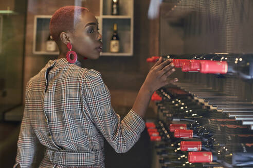 Young woman with short haircut choosing a wine in her cellar - VEGF01128