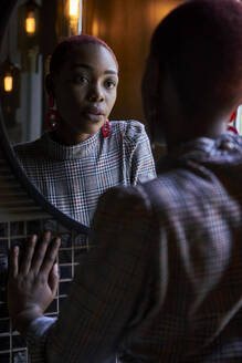 Black woman with short fun haircut looking to her reflection in a round mirror - VEGF01131