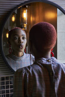 Young woman with short haircut looking to her reflection and sending a kiss in a round mirror - VEGF01134