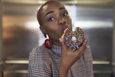 Young woman eating a doughnut in an elevator - VEGF01136