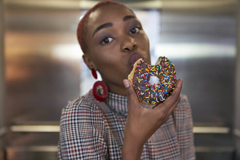 Junge Frau isst einen Doughnut im Aufzug - VEGF01136
