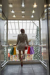 Frau mit bunten Einkaufstaschen im Aufzug und Blick auf einen Weihnachtsbaum - VEGF01146