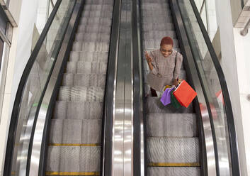 Junge Frau mit Einkaufstüten auf der Rolltreppe - VEGF01152