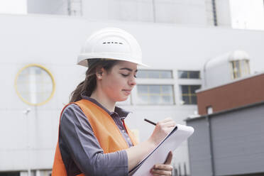 Female worker with clipboard taking notes at power plant - SGF02494