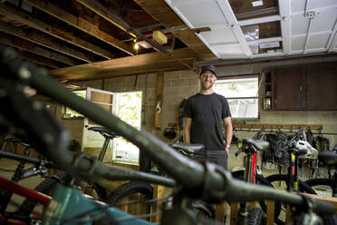 Low angle portrait of confident mechanic with hands in pockets standing in bicycle shop - CAVF70748