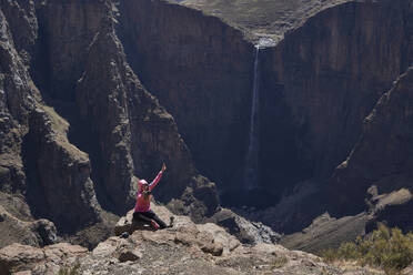 Glückliche Frau, die auf dem Gipfel eines Hügels an den Maletsunyane-Wasserfällen sitzt und ein Selfie macht, Lesotho - VEGF01163