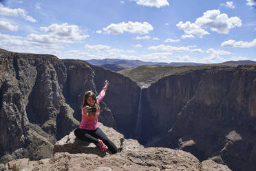 Glückliche Frau, die auf dem Gipfel eines Hügels an den Maletsunyane-Wasserfällen sitzt und ein Selfie macht, Lesotho - VEGF01164