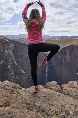 Frau balanciert auf einem Hügel bei den Maletsunyane Falls und genießt die Aussicht, Lesotho, lizenzfreies Stockfoto