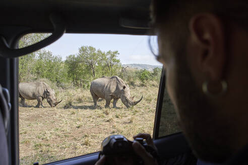 Mann fotografiert ein Nashorn aus dem Autofenster, Hluhluwe-Imfolozi Park, Südafrika - VEGF01181