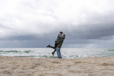 Russia, Kaliningrad Oblast, Zelenogradsk, Adult couple kissing on sandy coastal beach of Baltic Sea - EYAF00762