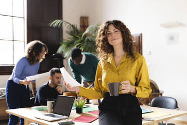 Portrait of a smiling woman in office with colleagues in background - FMOF00816