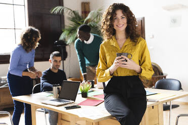 Portrait of a smiling woman in office with colleagues in background - FMOF00818