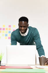 Smiling man working on laptop at desk in office - FMOF00833