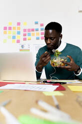 Man with laptop sitting at desk in office having lunch break - FMOF00838