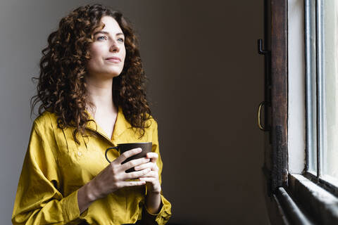 Woman looking out of window with coffee cup stock photo