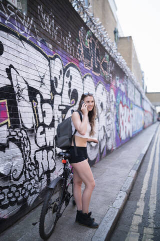 Smiling young woman on the phone at graffiti wall stock photo