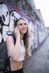 Smiling young woman on the phone at graffiti wall - FBAF01091