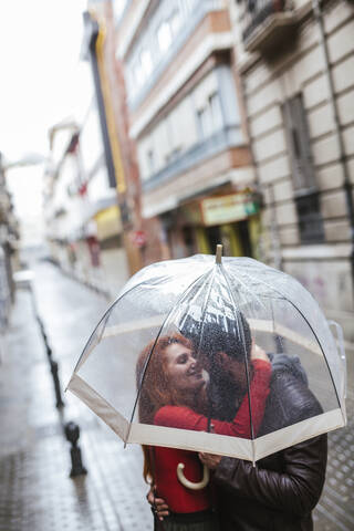 Verliebtes Paar küsst sich unter transparentem Regenschirm in der Stadt, lizenzfreies Stockfoto