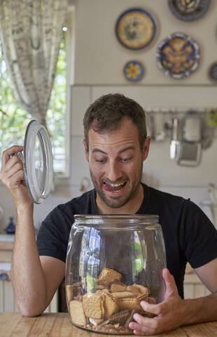 Man sitting in kitchen, looking in cookie jar, laughing stock photo