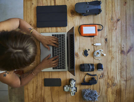 Person, die an einem Tisch mit Fotoausrüstung sitzt und einen Laptop benutzt, Blick von oben - VEGF01224