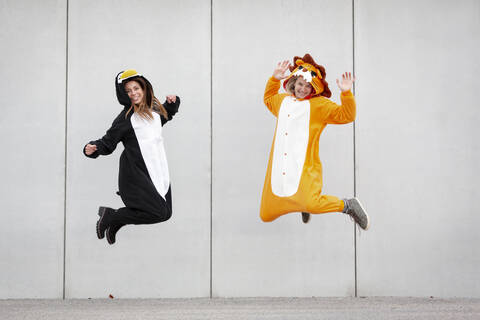 Zwei Frauen im Pinguin- und Löwenkostüm springen vor einer Betonwand, lizenzfreies Stockfoto