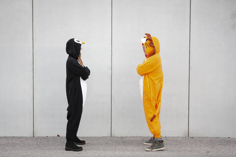 Zwei Frauen im Pinguin- und Löwenkostüm stehen sich vor einer Betonwand gegenüber, lizenzfreies Stockfoto